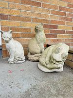 Group shot of all three concrete cat statues on outdoor surface