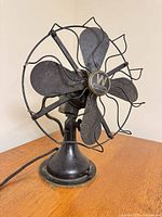 Front angled view of fan showing blades, cage, base, power cord