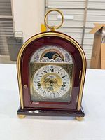 Front view of arched-top mantel clock showing dial, moonphase, mahogany case and brass trim