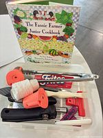 Overview of cookbook and utensils inside clear plastic box