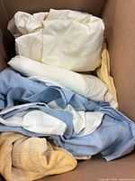 Box containing cream sheet, light blue curtain/pillow sham, yellow woven throw with fringe