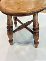 Top and legs of round wooden stool showing turned legs and cross stretcher