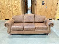 Front view of tan leather three-seat sofa showing cushions, rolled arms and nailhead trim