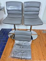 Two gray leather bar stools on chrome bases with extra seat/back in plastic