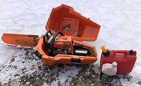 Chainsaw in open orange case with bar scabbard, manual, fuel can, oil bottle