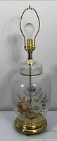Full view of lamp with harp, bulb, clear glass floral body, brass base