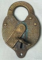 Front of Miller Lock Co. brass heart-shaped padlock showing maker’s mark and swinging cover