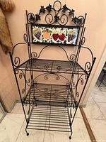 Full view of wrought iron baker's rack showing shelves and tile panel