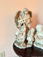 Tall guardian angel figurine with child and adjacent cherub with sunflower on round table