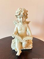 Front view seated cherub reading book with wings