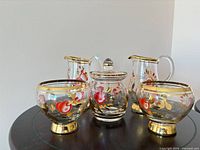 five-piece glassware set arranged together showing floral painting and gold trim
