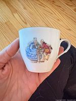 Teacup showing white porcelain, silver handle accent, Rococo couple motif transfer