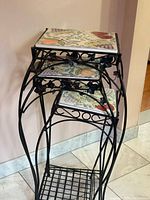 Three nesting plant stands stacked to show ceramic fruit motif tops and wrought iron frames
