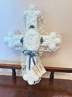 Front view of porcelain cross showing lace edging, blue ribbon roses, pearl trim, praying child medallion