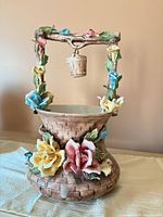 Front view of porcelain wishing well showing floral details and hanging bucket