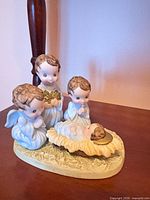 Front view of ceramic nativity figurine showing three child angels and infant Jesus