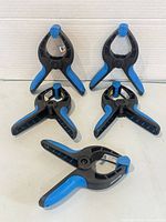 Five black and blue 2-inch spring clamps arranged on surface