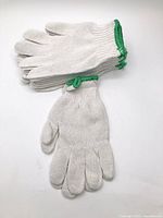 Stack of six pairs white knit gloves with green cuffs