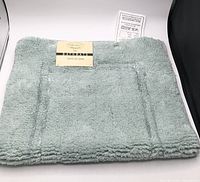 Full view of folded green bathmat with brand tag visible