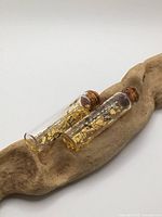 Two vials laying on driftwood showing overall appearance, corks, and gold flakes
