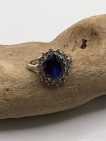 Front view of sterling silver ring with blue center stone and clear halo