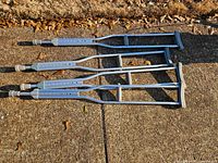 Four aluminum underarm crutches lying on pavement showing grips, tips and adjustment holes