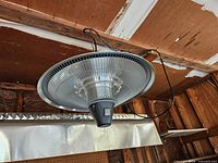 Hanging infrared heater with cord and chain mount visible above partial view of fluorescent shop light