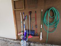 Overall view showing garden hose, cleaning tools, shovel, racket on wall
