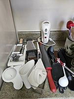 Stacked graters, mandoline slicer, rolling pin, can opener, white plastic attachments, handheld electric tool, assorted utensils