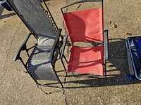Zero-gravity chair and red mesh beach chair set up on pavement