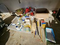 Overview of clear tote, cardboard box, brushes, dusters and cleaners on garage floor