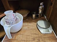 All items in cabinet: mixing bowl with measuring cups, digital scale, shaker, pitcher