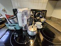 All items grouped on stovetop including pitcher, kettle, French press, sugar bowl, teacup, glass jar, basket with utensils