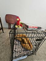 Overall view of black wire dog crate with brown plush toy inside, red/yellow plush toy and boxed collar on top
