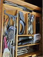 Drawer view showing assorted serving utensils, peeler, sharpener and flatware