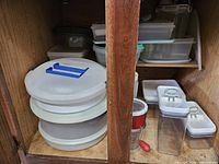 Stacked round cake carriers, clear canisters, red strainer and lids in cabinet