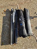 Two collapsed black folding light stands beside two black Pro Photo Studio carry bags