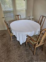 Round wood dining table covered with white cloth, four matching chairs around it