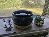 All items on windowsill: large green planter with saucer and inner pot, three metal key holders, stone plaque, small planter with succulent