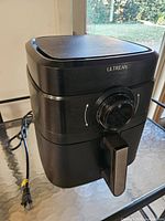 Front angled view of Ultrean black air fryer showing dial, handle, top touchscreen, power cord