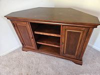 Three-quarter view of wooden corner TV cabinet showing two doors and open center shelves