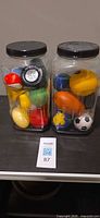 Two plastic jars filled with assorted stress balls and squishy toys, lid detail and variety of shapes visible