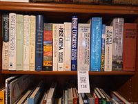 Shelf showing assorted hardcover and paperback books listed