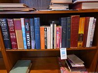 Books arranged upright on a wooden shelf with a few stacked horizontally; spine titles partially readable