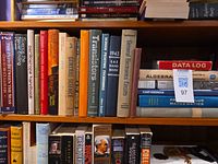 Shelf with top row of engineering and science books including schematic diagrams, Path Between the Seas, oscilloscope handbook, etc.
