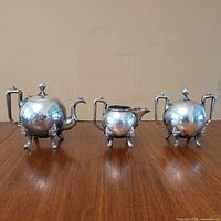 Three views of spherical silver-plated teapot on lion feet