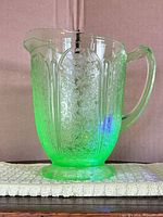 Side view of uranium glass pitcher showing embossed floral pattern and glow