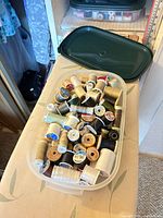 Top view of plastic container filled with numerous thread spools and dark green lid