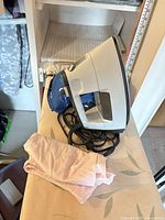 Side view of iron with cord, pink cloth and blue pad