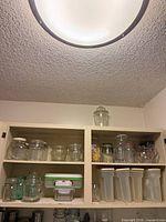 Cabinet showing assorted glass jars on top shelf and plastic canisters below